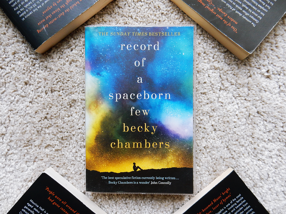 A photo of the paperback version of "Record of a Spaceborn Few" on a beige carpet.